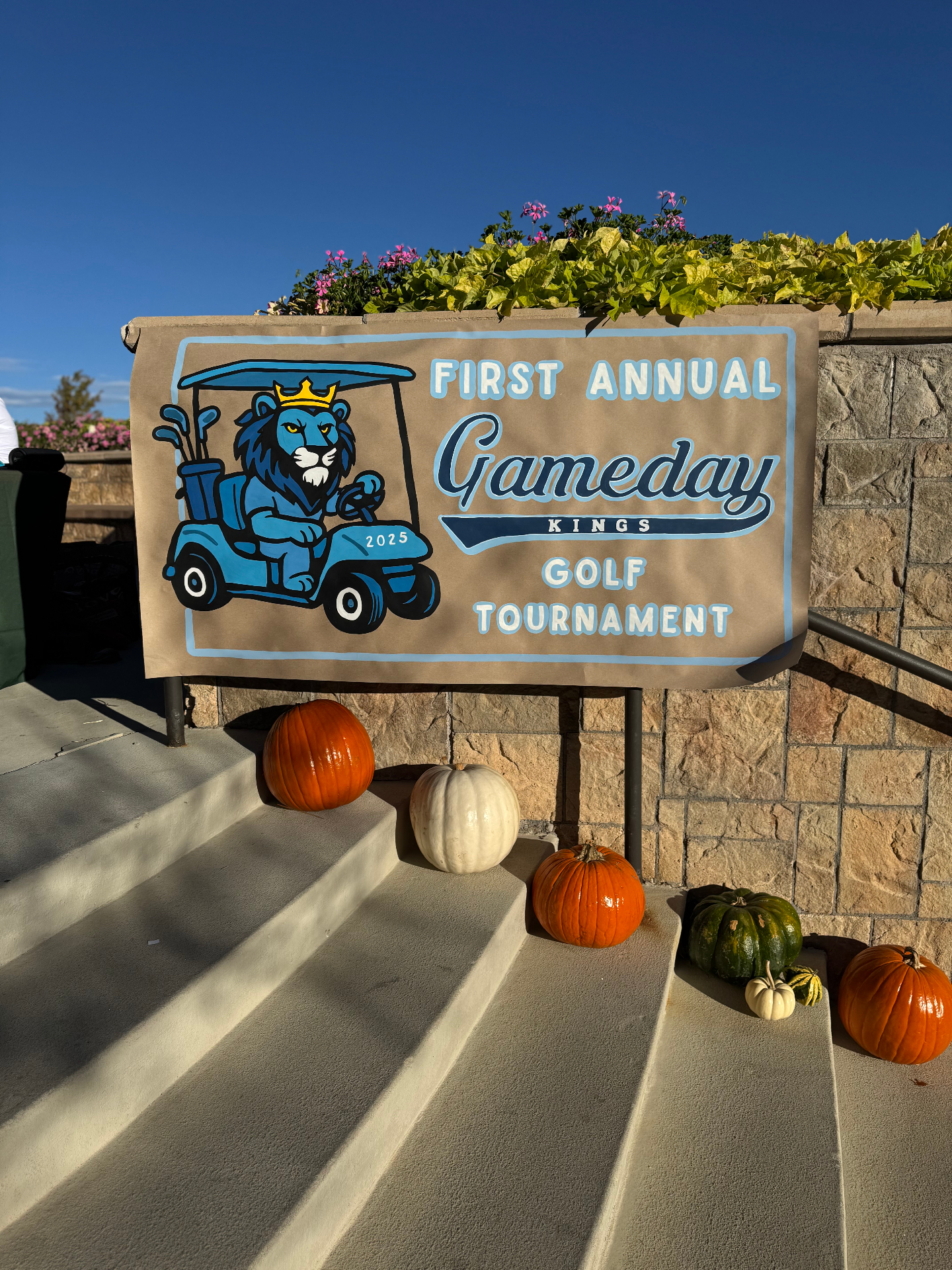 Hand-painted banner from the First Annual Gameday Kings Golf Tournament featuring a lion driving a golf cart